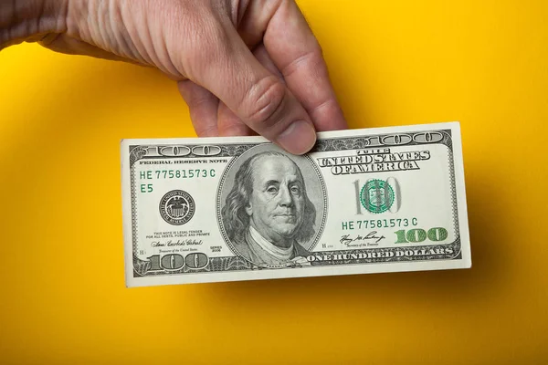 Honderd dollars in de hand op een gele achtergrond. — Stockfoto