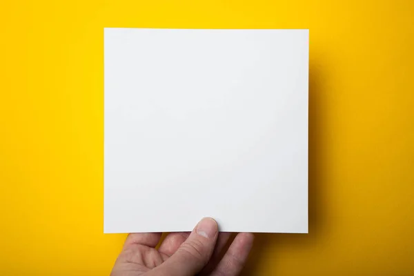 Čtvercové uspořádání bílého papíru v ruce na žluté poza — Stock fotografie