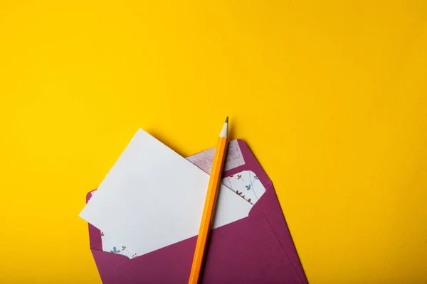 Envelop, wit vel papier en potlood op een gele achtergrond — Stockfoto