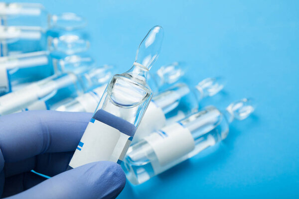 A hand in a blue glove holds an ampoule.