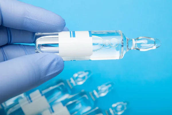 Närbild av ampull i handen på blå bakgrund, vaccination. — Stockfoto