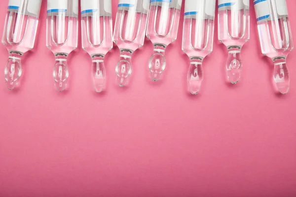 Cosmetic preparations in ampoules on a pink background. Copy spa