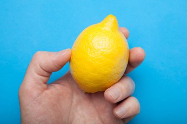 Bir adamın elini sulu sarı limon mavi bir arka plan üzerinde tutar..