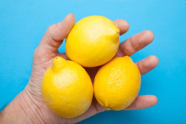 Elinde üç büyük limon mavi bir arka plan üzerinde izole