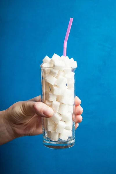 Un bicchiere pieno di cubetti di zucchero bianco in una mano . — Foto Stock