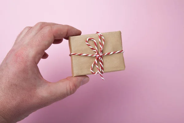 A mão segura uma pequena caixa de presente caseira em um fundo rosa . — Fotografia de Stock