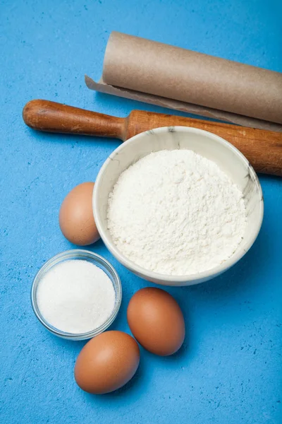 Flour, eggs, butter, sugar on a blue background, vertically.