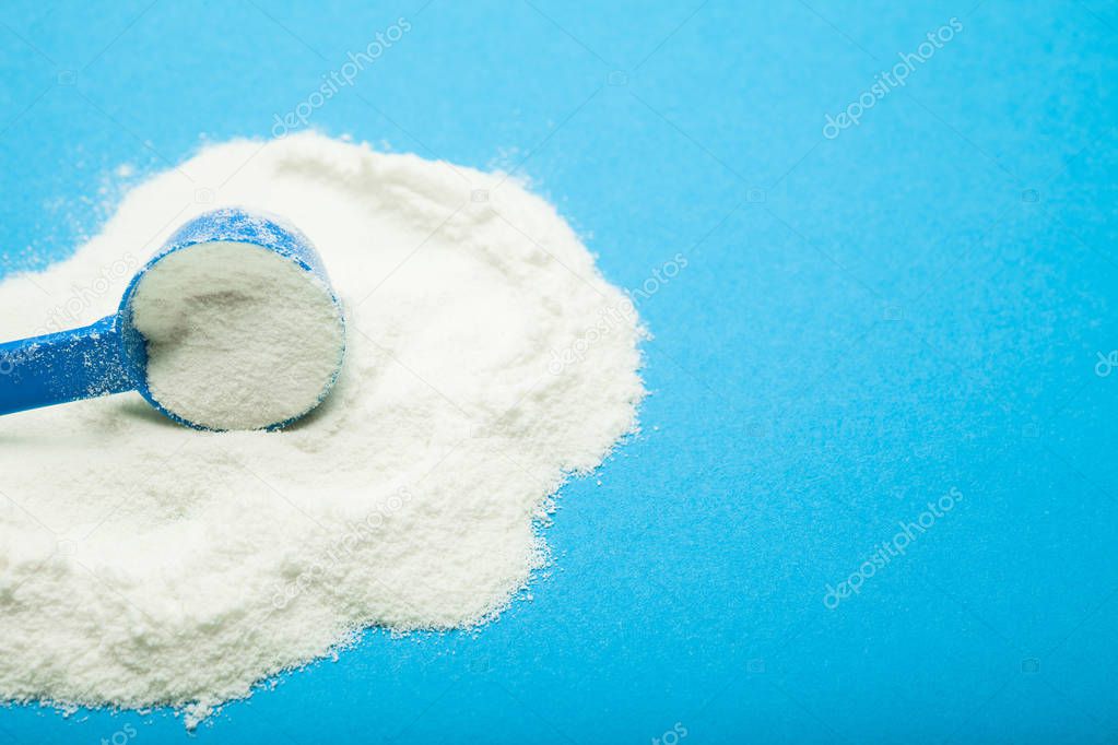 Plastic spoon with milk powder on a blue background, empty space