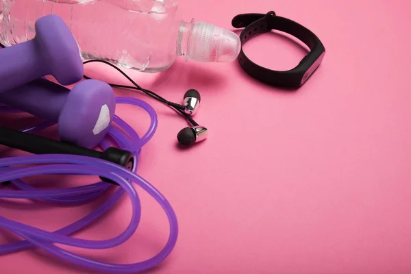 Sport and athletics, dumbbell and skipping rope with a fitness bracelet on a pink background. Copy space for text.