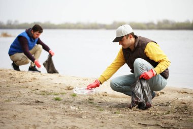 Adam gönüllü olarak sahildeki çöpleri kaldırıyor. Sahil çevre kirliliği, açık hava çöplüğü ve çöp..