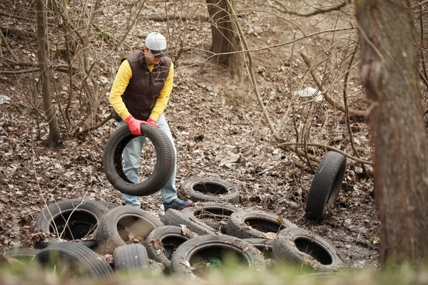 Volunteer removes car tires from the park. Environmental pollution, outdoor trash and rubbish.