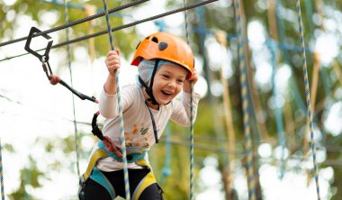 Miğferli küçük kız dışarıdaki macera parkında iplere tırmanıyor. Olağanüstü spor, doğada aktif eğlence..
