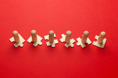 Takım oluşturmanın sembolü olarak kırmızı arkaplandaki yapbozların tahta figürleri. Organizasyon grubu insanları iş başında. İşbirliği ve ortaklık.