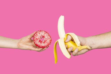 Erotic banana and donut in the hands as a symbol of the penis and vagina isolated on a pink background. The relationship between a man and a woman, sex and passion.