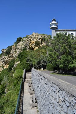Deniz deki bir dağın tepesinde beyaz ve gri deniz feneri.