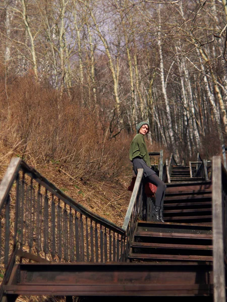 一个穿着灰色裙子和裤袜的女人，戴着一顶绿色的帽子，正坐在长长的楼梯的栏杆上。. — 图库照片