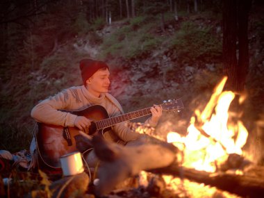 Camping at night around a campfire in nature to the sound of a guitar.