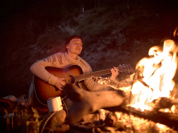Camping at night around a campfire in nature to the sound of a guitar.