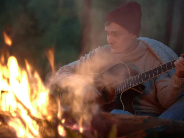 Camping at night around a campfire in nature to the sound of a guitar.