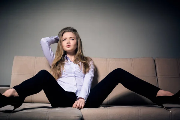 Güzel bir sarışın pantolon ve bir gömlek bej kanepede oturuyor.