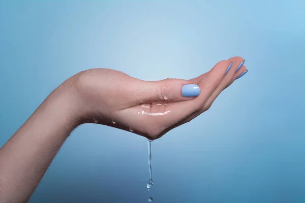 Un'immagine della mano di una donna su cui scorre l'acqua, su uno sfondo blu — Foto Stock