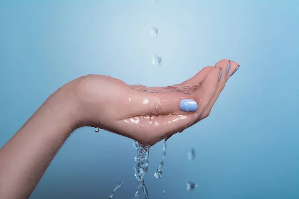 Uma imagem da mão de uma mulher na qual a água flui, sobre um fundo azul . — Fotografia de Stock