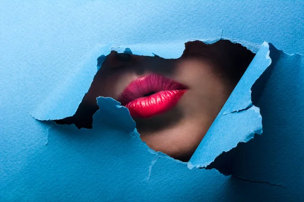 Una vista delle labbra femminili attraverso un buco in uno sfondo blu carta — Foto Stock