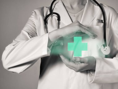 Female doctor holds a pictogram of a green cross in his hands. clipart