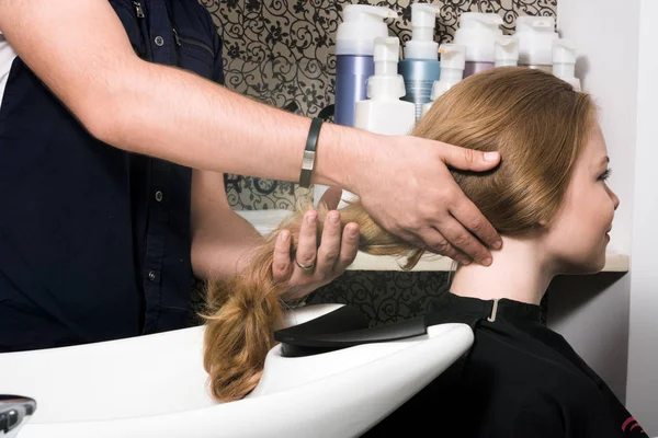 Una joven se prepara para lavarse la cabeza en un salón de belleza . — Foto de Stock