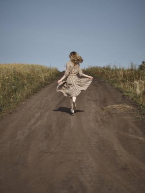 Sarışın arkadan çizgili bir elbise ile bir ülke yolda aşağı çalışır