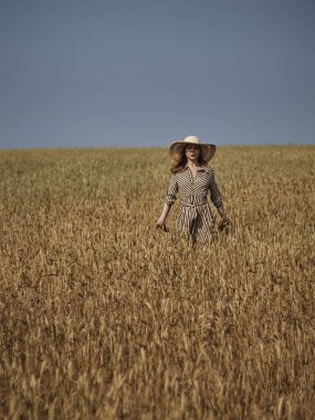 Buğday tarlasında ki bir sarışın hasır şapka ve dikey çizgili bir elbiseyle yürüyor..