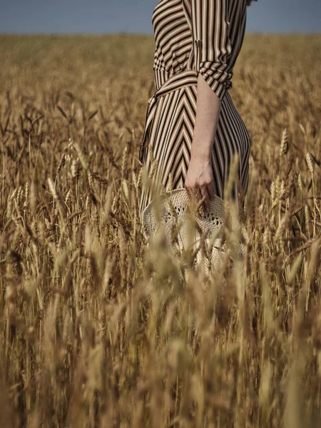 Una chica con un vestido a rayas lleva un sombrero de paja en la mano en primer plano . —  Fotos de Stock