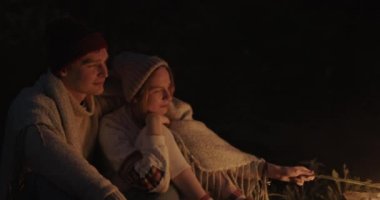 Genç bir çift ormanda geceleri oturur, bir şenlik ateşi önünde ortak bir ekose altında kucaklayan, konuşma ve gülerek.