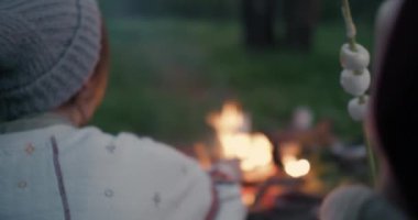 Genç bir çift bir dağ nehrinin kıyısında bir ormanda oturur, sohbet ve marshmallow kızartma.