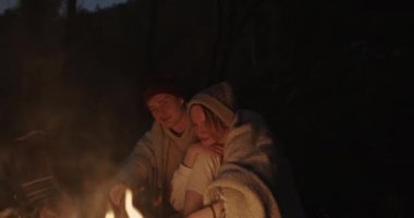 Genç bir çift ormanda geceleri oturur, bir şenlik ateşi önünde ortak bir ekose altında kucaklayan, konuşma ve gülerek.