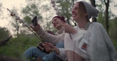 Genç bir çift ateşin yanında oturur, marshmallow kızartılır, yüksek sesle güler ve eğlenir..