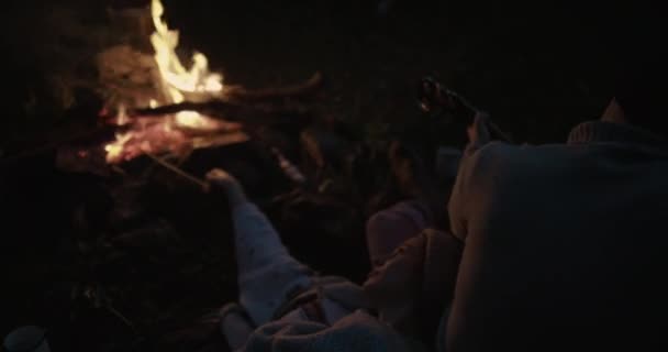 Um jovem casal senta-se à noite junto à lareira. O cara toca guitarra e sua namorada se deita em seu colo e ouve música . — Vídeo de Stock