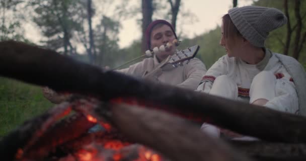 Genç bir çift ateşin yanında oturur, lokum ları kızartın, konuşup gülerler.. — Stok video
