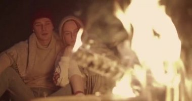 Genç bir çift ormanda geceleri oturur, bir şenlik ateşi önünde ortak bir ekose altında kucaklayan, konuşma ve gülerek.