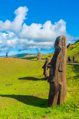 Moais yakınındaki bir yol bir hill tarafından; turistler tarafından arka planda yürümek.