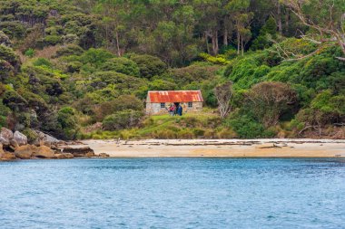 Stewart Island, Yeni Zelanda--22 Şubat 2018. Dört kişilik bir grubun Stewart Adası bir ormandaki küçük bir taş evin dışında duruyor. Yalnızca içerik kullanımı.
