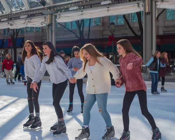 Reston, Va Usa--17 Kasım 2018. Dört genç kadın buz pateni Reston şehir merkezinde rink vardır; iki dengelemek için bir arkadaşa yardım etmekle.