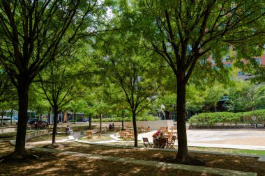 Reston, VA, ABD -- 17 Temmuz 2020. Reston Şehir Merkezi Parkı 'ndaki insanlar sosyal olarak ağaçların gölgesinde uzaklar..