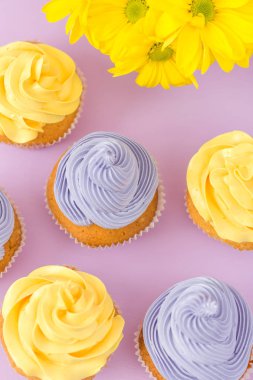 Cupcakes sarı ve mor krem ve Kasımpatı Menekşe pastel zemin üzerine süslenmiş. Boşaltmak alan. Tebrik için kullanılabilir anneler gün ve Sevgililer kartı. Minimalizm kavramı.