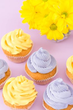 Cupcakes sarı ve mor krem ve Kasımpatı Menekşe pastel zemin üzerine süslenmiş. Boşaltmak alan. Tebrik için kullanılabilir anneler gün ve Sevgililer kartı. Minimalizm kavramı.