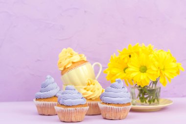 Cupcakes sarı ve mor krem ve Kasımpatı Menekşe pastel zemin üzerine süslenmiş. Boşaltmak alan. Tebrik için kullanılabilir anneler gün ve Sevgililer kartı. Minimalizm kavramı.