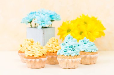 Kekler retro eski püskü şık vazoda sarı ve mavi krizantem pastel zemin üzerine krema ile dekore edilmiştir. Tebrik kartı minimalizm natürmort kavram için tatlı ekmek.