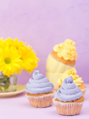 Cupcakes sarı ve mor krem ve Kasımpatı Menekşe pastel zemin üzerine süslenmiş. Boşaltmak alan. Tebrik için kullanılabilir anneler gün ve Sevgililer kartı. Minimalizm kavramı.