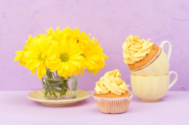 Cupcakes sarı krem ve Kasımpatı Menekşe pastel arka plan üzerinde buket süslenmiş. Tebrik için kullanılabilir anneler gün ve Sevgililer kartı. Minimalizm kavramı. Boşaltmak alan.