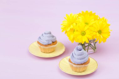 Cupcakes mor krem ve menekşe pastel zemin üzerine sarı Kasımpatı buket ile dekore edilmiştir. Metin alanı. Tebrik için ideal anneler gün ve Sevgililer kartı. En az natürmort kavramı.